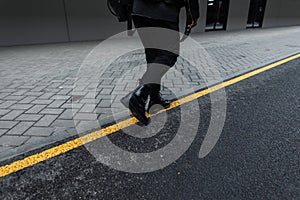 Fashion young man in a stylish jacket in vintage jeans in leather fashionable boots with a trendy black backpack is walks on the