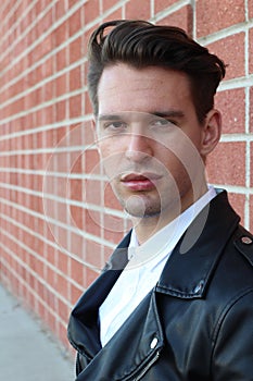 Fashion young man in white shirt and black leather jacket over modern blurred brick wall