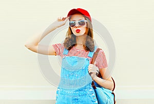 Fashion young pretty woman wearing a denim jumpsuit with baseball cap and sunglasses over white