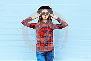 Fashion young woman model wearing black hat, red checkered shirt over blue background