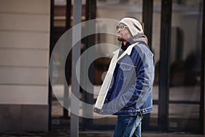 Fashionable African american man model wearing stylish outfit denim jacket, hat, hoodie and sunglasses walking in city