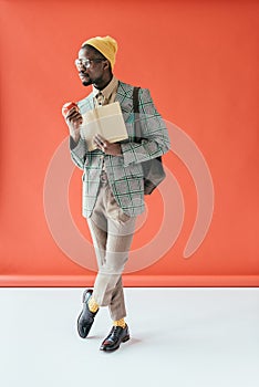 fashionable african american man posing with book and apple