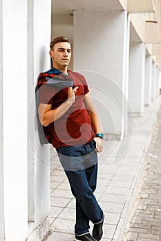 Fashionable american young man in red t-shirt in a checkered colorful fashionable shirt in trendy jeans in sneakers posing on the