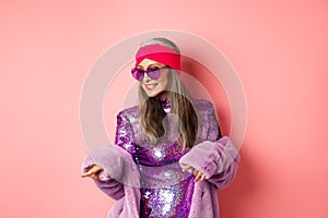 Fashionable asian senior woman dancing disco, wearing glittering shiny dress and heart-shaped sunglasses, having fun