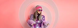 Fashionable asian senior woman dancing disco, wearing glittering shiny dress and heart-shaped sunglasses, having fun