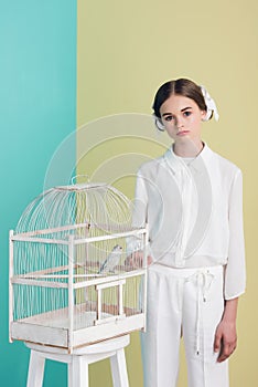 fashionable attractive girl in white outfit with parrot in cage on turquoise