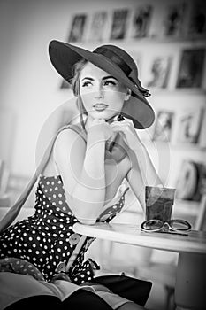 Fashionable attractive lady with hat and scarf sitting in restaurant, indoor shot. Young woman posing in elegant scenery