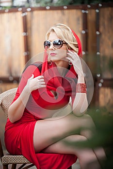 Fashionable attractive lady with red dress and headscarf sitting on chair in restaurant, outdoor shot in sunny day.