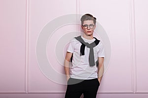 Fashionable attractive young man model in vintage glasses with a hairstyle in a trendy white t-shirt in black jeans with a nose