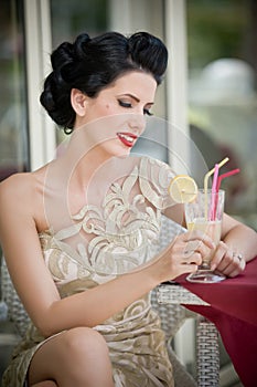 Fashionable attractive young woman in lace dress sitting in restaurant, beyond the windows. Beautiful brunette posing