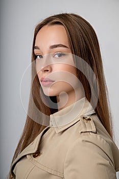 Fashionable beautiful girl posing in classic trench coat with long dark hair posing in a classic trench coat, on a white