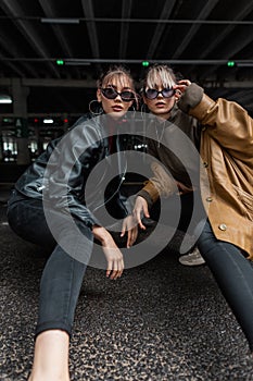 Fashionable beautiful two women models with stylish leather jacket and sweater with black jeans posing in the city