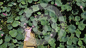 fashionable beautiful woman in a pink dress is lying on a boat in blooming lotuses in summer. drone point of view.