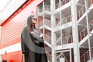 Fashionable beautiful young attractive woman with stylish sunglasses in trendy green coat with gray sweater posing in the city.