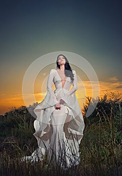 Fashionable beautiful young woman in white bridal long dress posing outdoor
