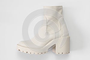 Fashionable beige leather women`s boots with rough sole on light gray background top view. Trendy spring autumn shoes. Creative