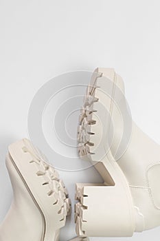 Fashionable beige leather women`s boots with rough sole on light gray background top view. Trendy spring autumn shoes. Creative