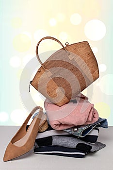 A fashionable brown luxury oak cork women`s handbag on a pile of folded women`s clothing and a single shoe on the table over