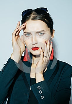 Fashionable brunette woman posing in trendy look. Black jacket, black swimsuit, sunglasses and red earrings.