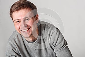 Fashionable casual smiling young man with light beard, on gray b