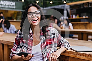 Fashionable caucasian girl with smartphone posing in cafe with smile. Gorgeous female student sitti