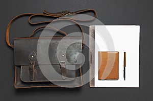 Fashionable concept. Brown leather men`s bag, wristwatch, leather passport cover, pen, blank white sheets on black background top