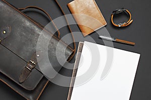 Fashionable concept. Brown leather men`s bag, wristwatch, leather passport cover, pen, blank white sheets on black background top