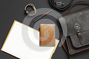 Fashionable concept. Brown leather men`s bag, wristwatch, leather passport cover, pen, blank white sheets on black background top