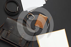 Fashionable concept. Brown leather men`s bag, wristwatch, leather passport cover, pen, blank white sheets on black background top