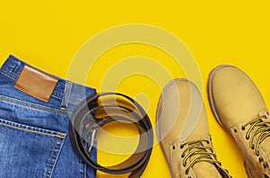 Fashionable concept. Men`s casual wear, yellow work boots from natural nubuck leather, blue jeans and brown belt on bright yellow