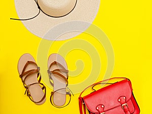Fashionable concept. Women`s beach hat, red handbag, sandals. Yellow background, top view