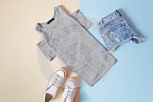 Fashionable concept. Women`s urban style. Gray T-shirt, white sneakers and jeans shorts on a soft blue background