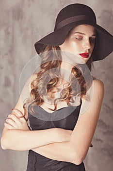Fashionable confident woman with long legs in black sexy bodysuit,  posing in studio with beton background. Girl in hat