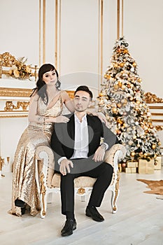 The fashionable couple, a handsome man in a black suit and a young woman in a gold evening dress sitting together in a