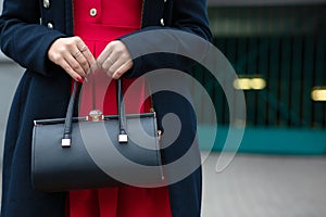 Fashionable dressed girl holding black leather purse. Empty space