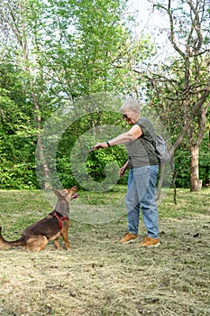 Fashionable elderly woman playing with her dog in the park.