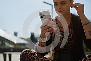 Young woman in leopard clothes listening to music in headphones and browsing an application on a modern smart phone. Tattooed