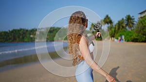 Fashionable female travel vlogger records beach guide with pro camera, wireless lav mic. Sunlit coast as backdrop