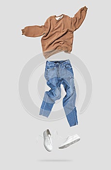 Fashionable flying brown cotton stylish sweatshirt, blue jeans, leather sneakers isolated on gray background. Clothes, shoes,