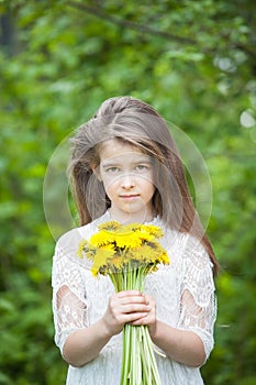 Fashionable girl in a beautiful white dress poses with yellow dandelion flowers