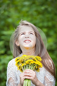 Fashionable girl in a beautiful white dress poses with yellow dandelion flowers