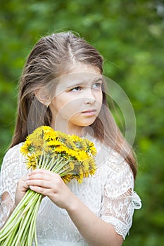 Fashionable girl in a beautiful white dress poses with yellow dandelion flowers
