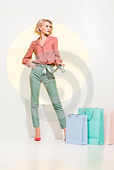 Fashionable girl posing near shopping bags on white with yellow circle