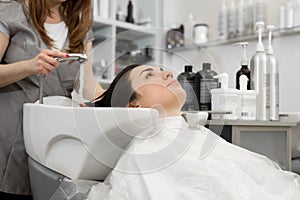 Fashionable hairdresser washes away shampoo and foam with water from girl& x27;s hair.