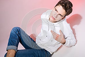 Fashionable handsome young European male model dressed in white sweatshirt, blue jeans and white sneakers posing in studio on a