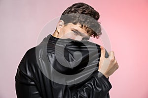 Fashionable Handsome young man in leather jacket posing in the studio against the background of the wall. Portrait of a young gay