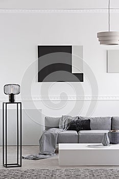 Fashionable industrial black lamp next to scandinavian sofa in bright living room