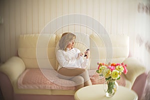 A fashionable lady dressed in a white blouse and beige trousers. A young woman uses a mobile phone indoors with an
