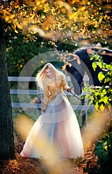 Fashionable lady with white bridal dress near black horse in forest.