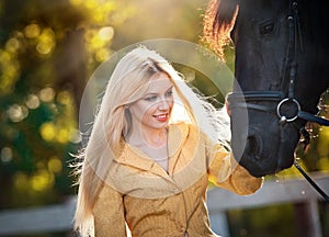 Fashionable lady with yellow coat near black horse in forest.